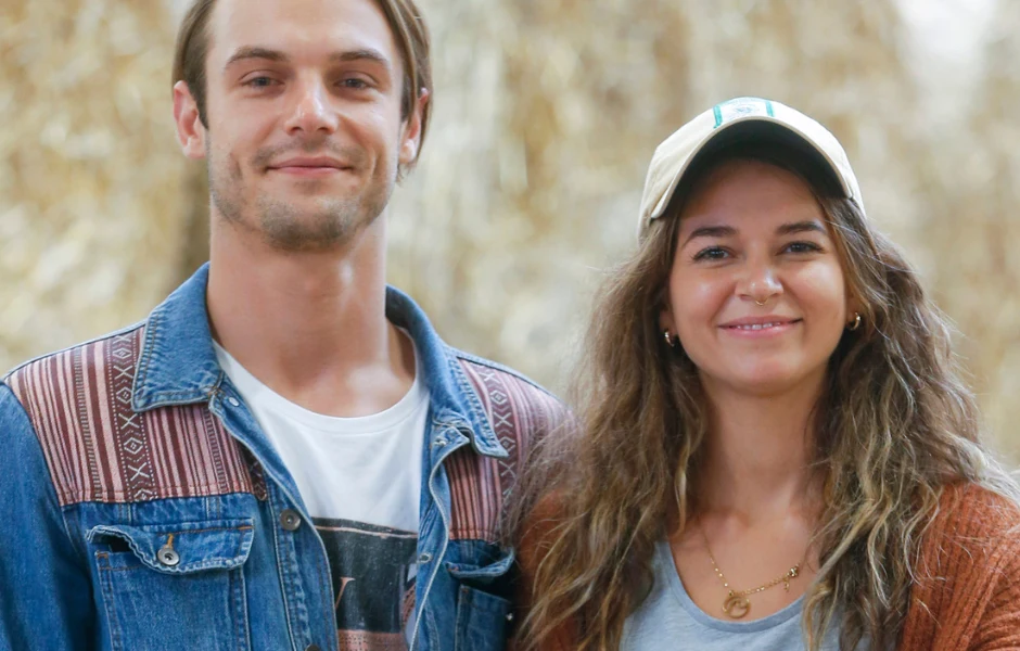 Mateusz Rzeźniczak, Karolina Sawka Młody mężczyzna w dżinsowej kurtce i kobieta z długimi włosami, ubrana w czapkę z daszkiem i naszyjnik, stoją obok siebie i uśmiechają się do obiektywu.
