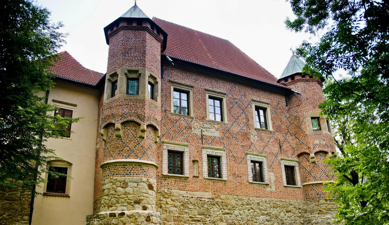 Zamek w Dębnie niedaleko Tarnowa Zamek w Dębnie z czerwonej cegły, z dwiema cylindrycznymi wieżami, otoczony kamiennym murem u podstawy.
