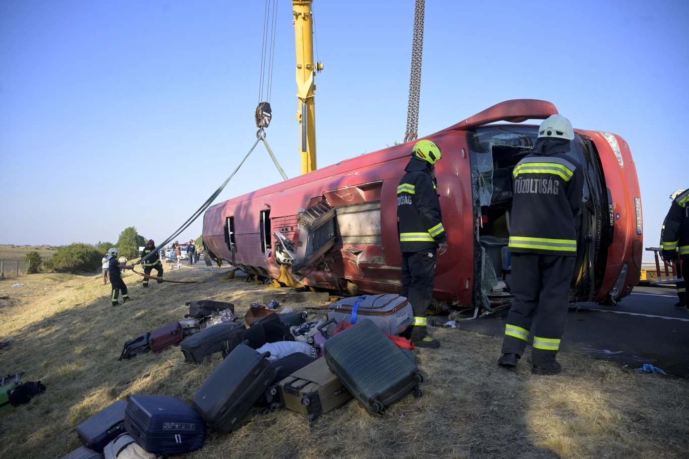 Wypadek polskiego autokaru na Węgrzech. Adwokat: Kierowca jest w stanie szoku Ratownicy i strażacy przy przewróconym autokarze, dookoła walizki i bagaże, w tle dźwig