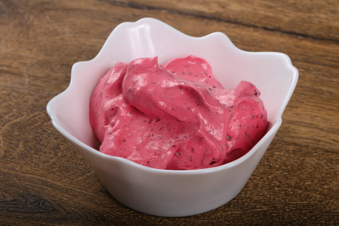 Czy mrożony jogurt to lepszy wybór niż lody? Mrożony jogurt o kremowej konsystencji i musie malinowym w białej miseczce na drewnianym blacie.