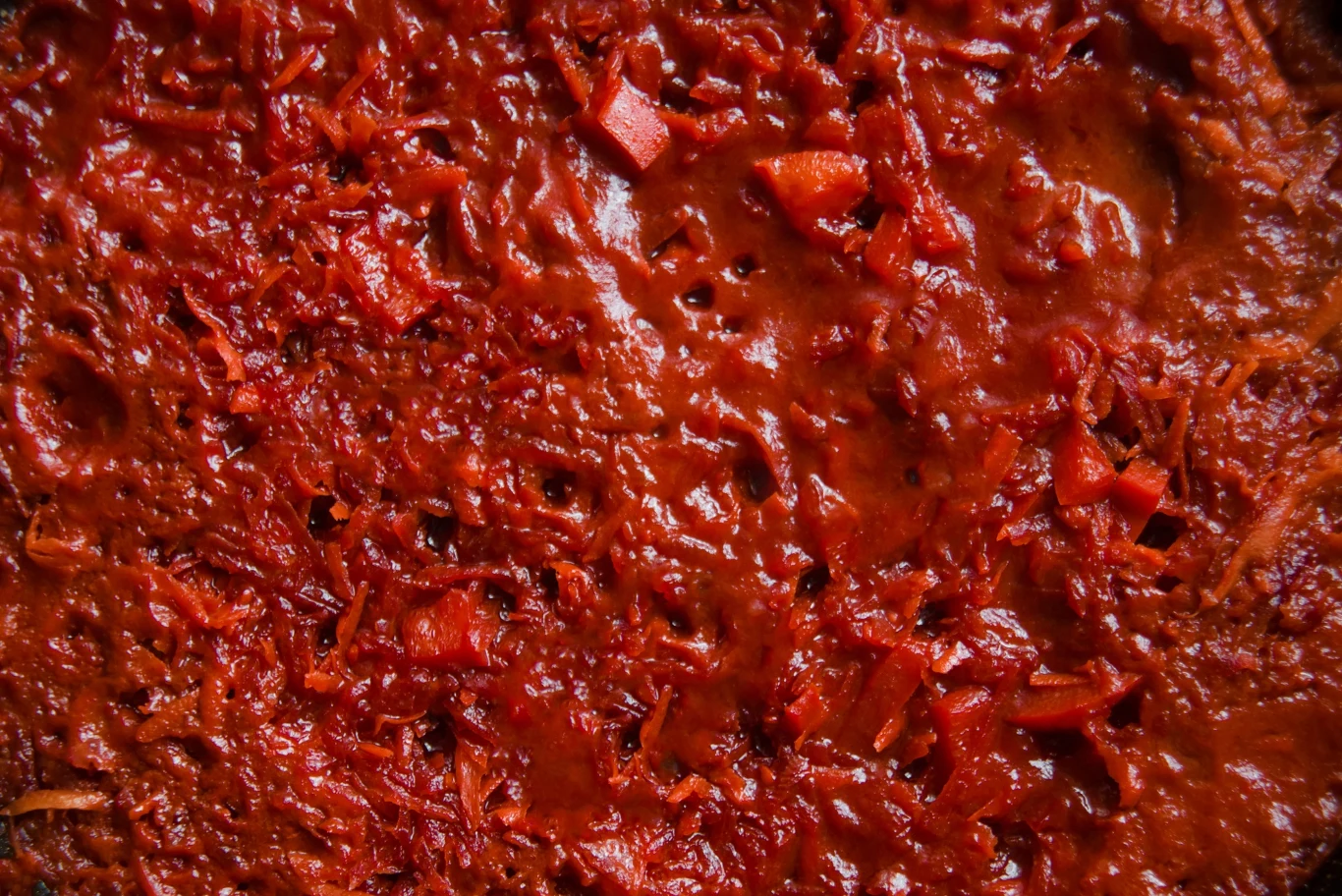 Passata albo przecier smakują lepiej z domowych pomidorów Gęsty sos o intensywnie czerwonej barwie z widocznymi kawałkami papryki i startego buraka, sugerujący obecność podstawowych składników gulaszu lub leczo warzywnego.