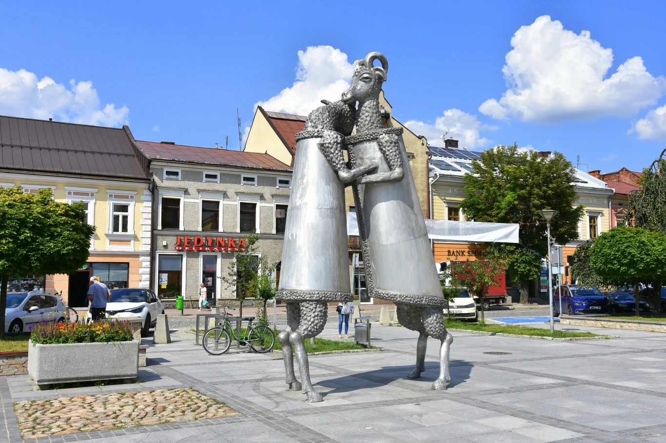 Rynek w Nowym Targu i rzeźba "Dialog" autorstwa Michała Batkiewicza Rynek w Nowym Targu z metalową rzeźbą „Dialog” Michała Batkiewicza na tle kamienic i zieleni.