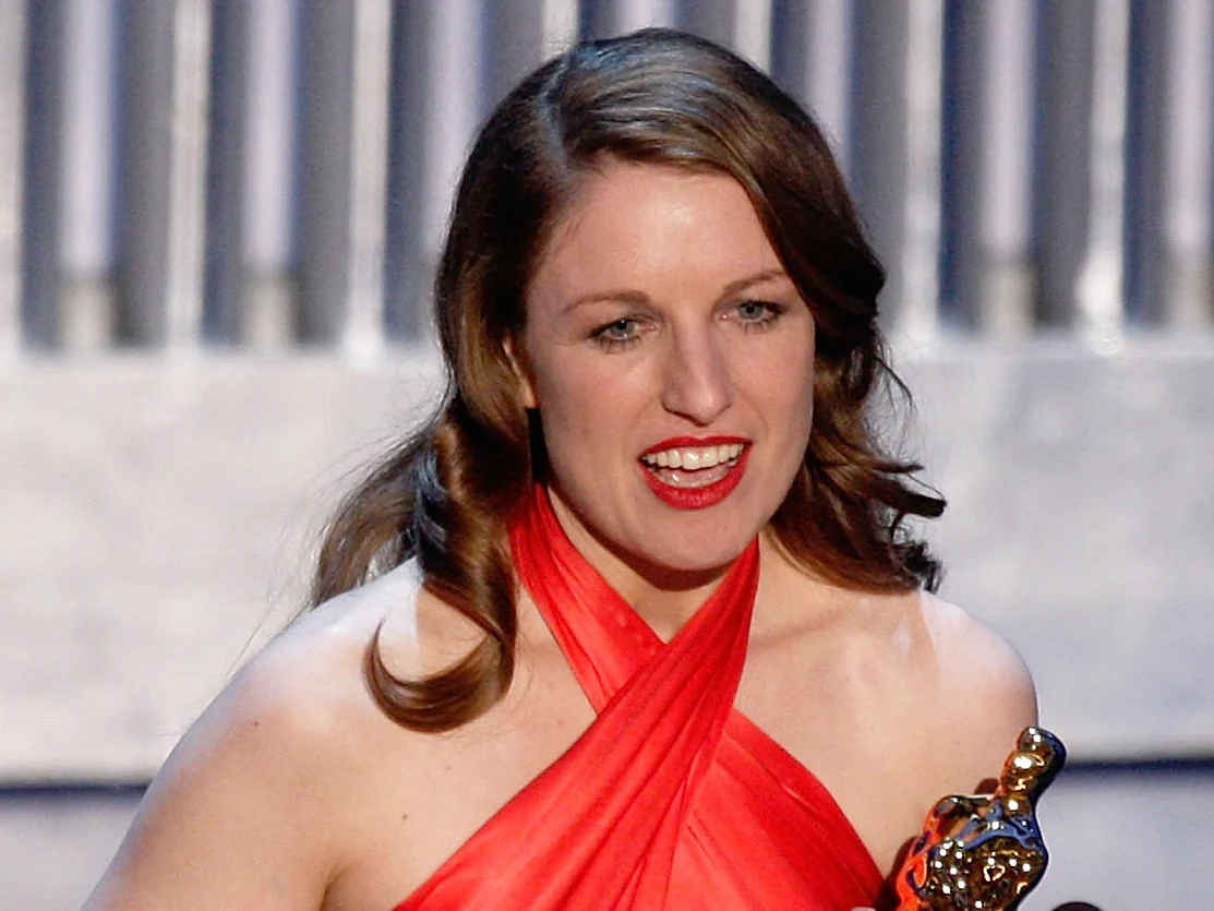 Suzie Templeton podczas gali rozdania Oscarów w 2008 roku Suzie Templeton w czerwonej sukni ze statuetką Oscara, gala Oscarów 2008, jasne pionowe panele w tle.