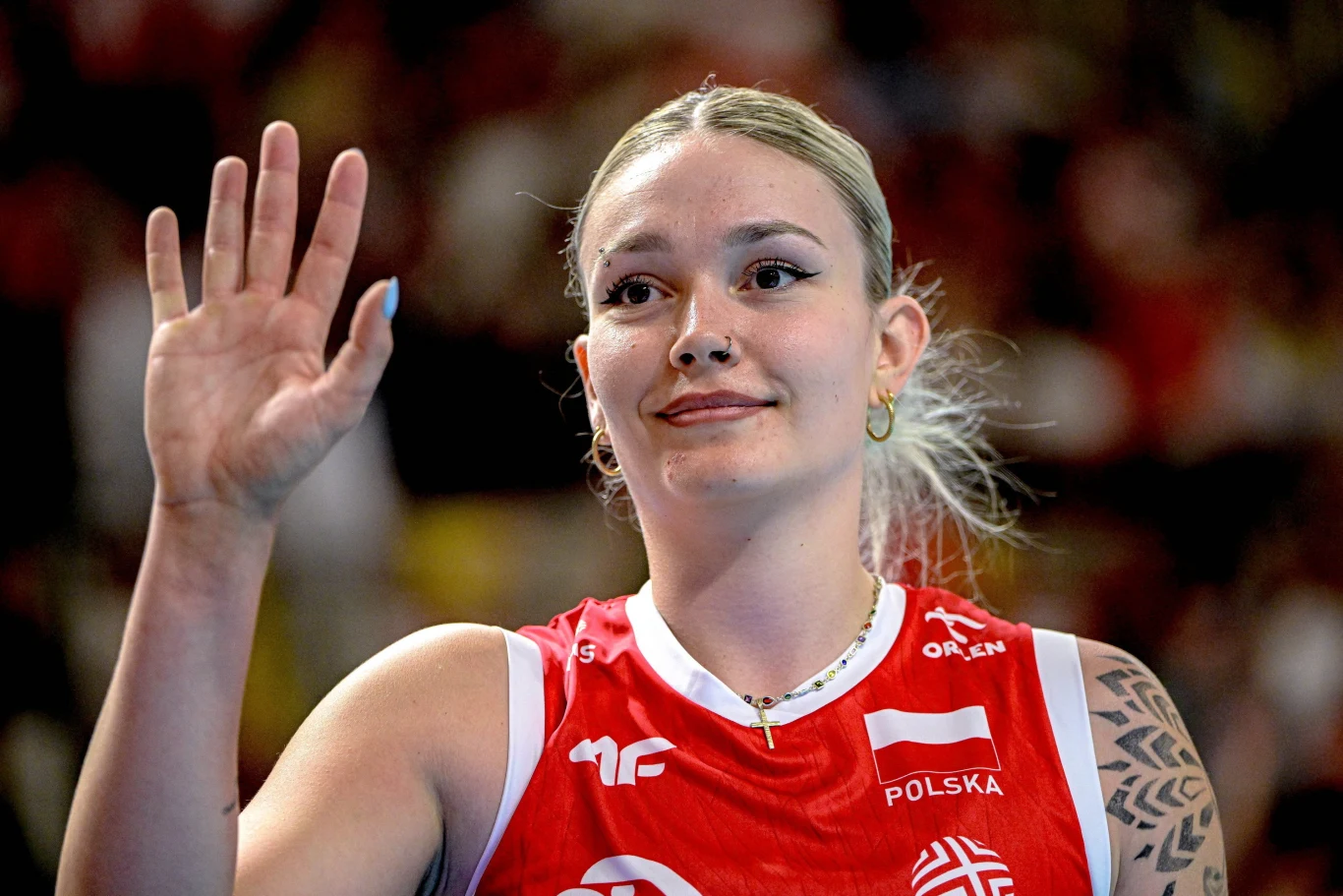 Julia Szczurowska Julia Szczurowska w czerwonym stroju reprezentacji Polski, z uniesioną ręką, na tle publiczności.