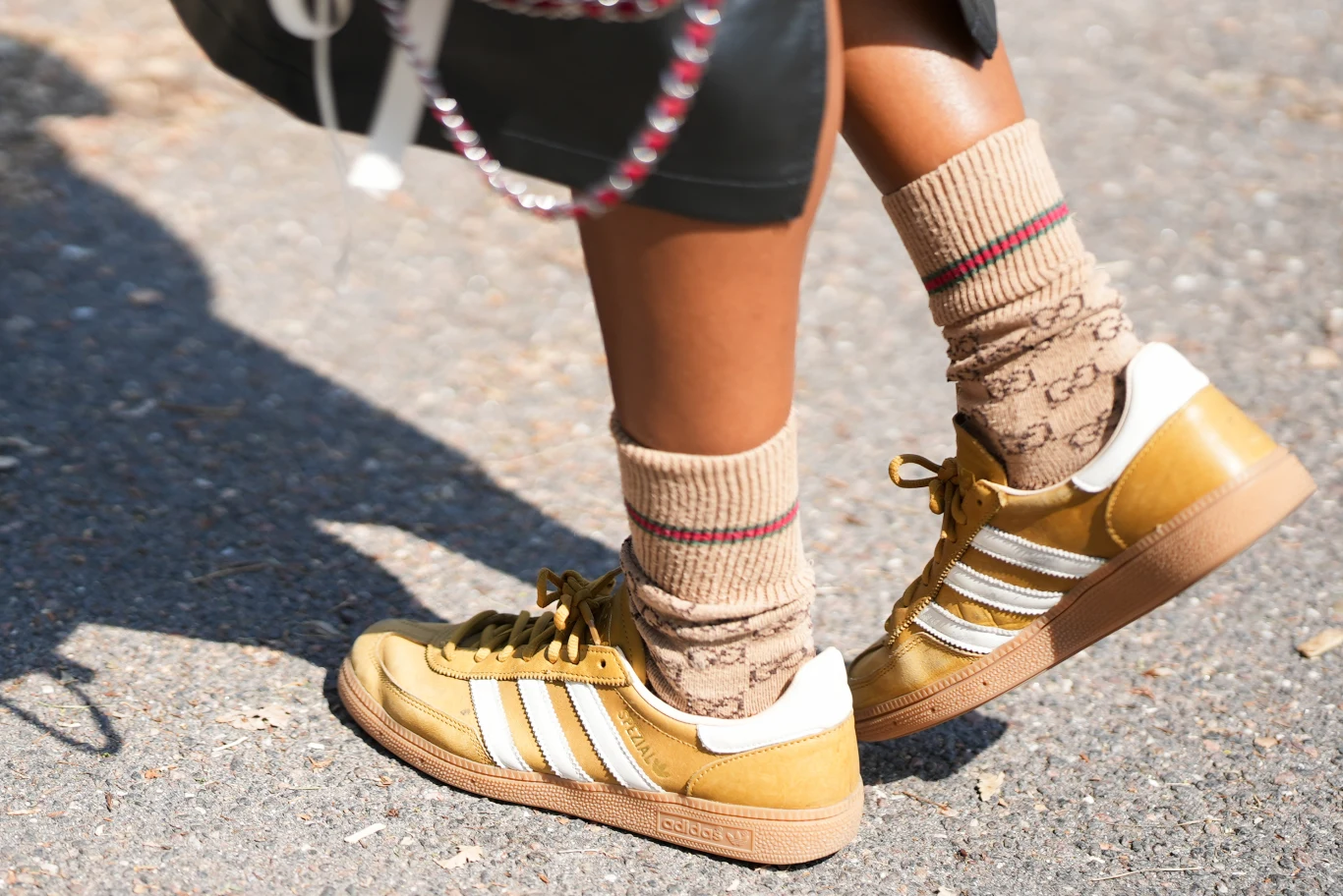 Musztardowy kolor wkradł się na ubrania, dodatki, a nawet buty Żółte sneakersy Adidas z białymi paskami połączone z beżowymi skarpetkami Gucci ozdobionymi charakterystycznym logo.