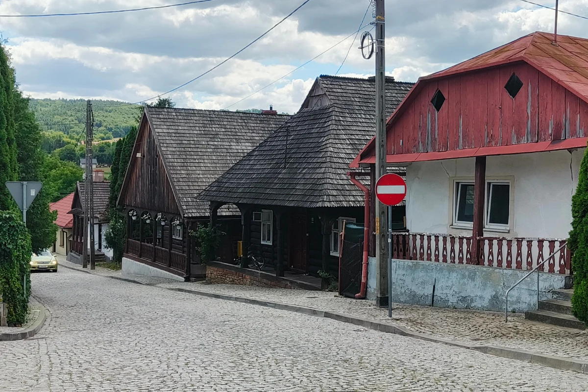 Kamienne, pochyłe uliczki z drewnianymi i murowanymi domami o tradycyjnych dachach, znak zakazu wjazdu oraz otaczająca zieleń podkreślająca spokojny charakter małego miasteczka.