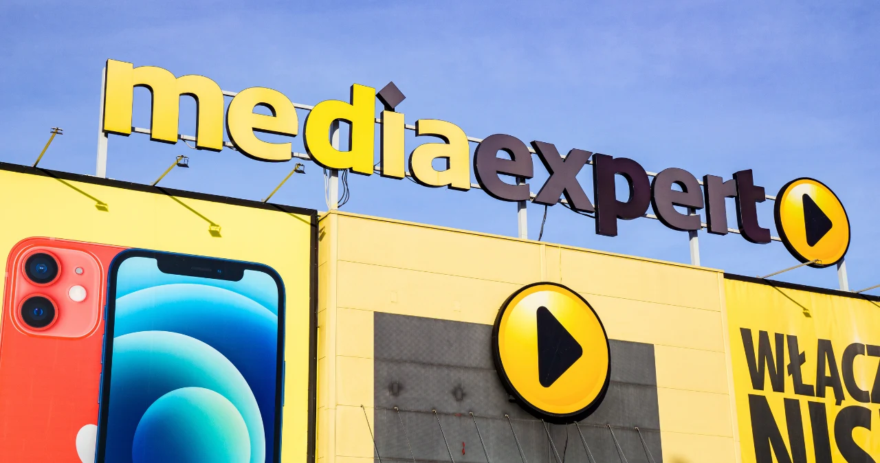 TOP 7 gadżetów z Media Expert dla ucznia. Mogą ułatwić naukę w szkole Logo i szyld Media Expert na żółtym tle, reklama smartfona oraz czarny trójkątny przycisk na okręgu.