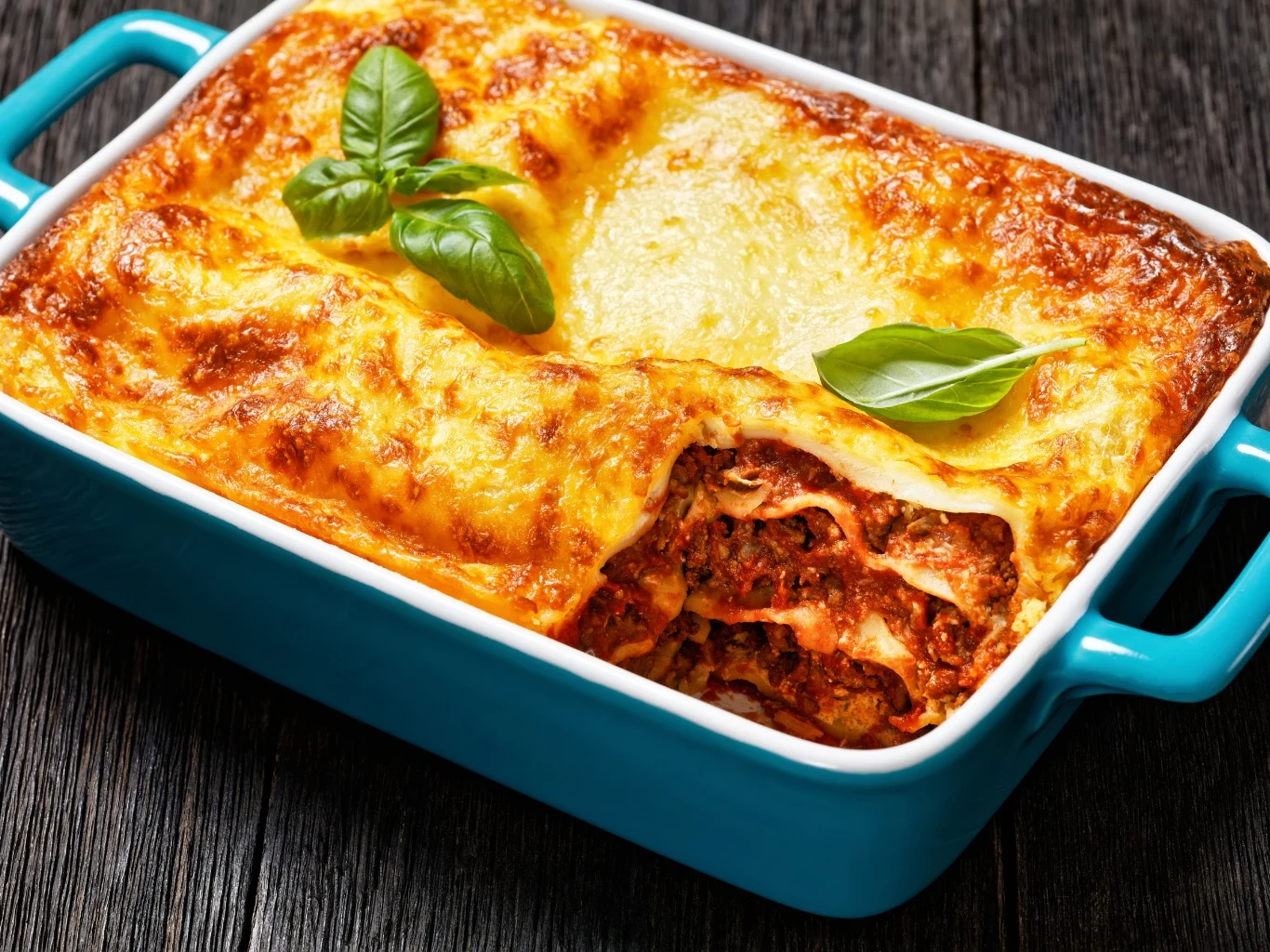 Tradycyjna, włoska lasagne. Zapiekanka lasagne z warstwami makaronu, mięsa, sosu pomidorowego i roztopionym serem, udekorowana świeżą bazylią.