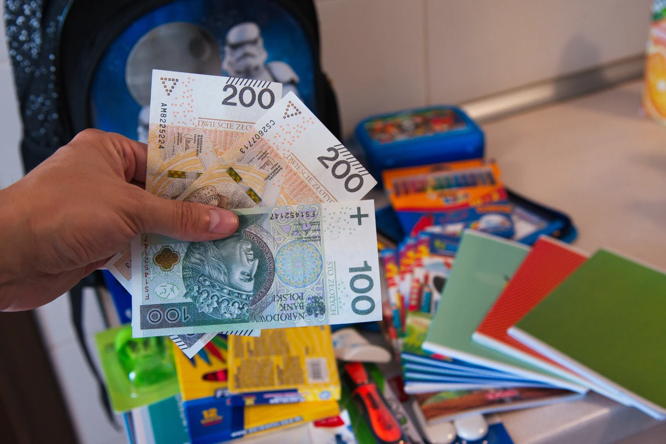 Czy wydatki na wyprawkę szkolną można odliczyć od podatku? Ręka rodzica z pieniędzmi płacącymi za zakup artykułów szkolnych na wyprawkę dla dziecka.