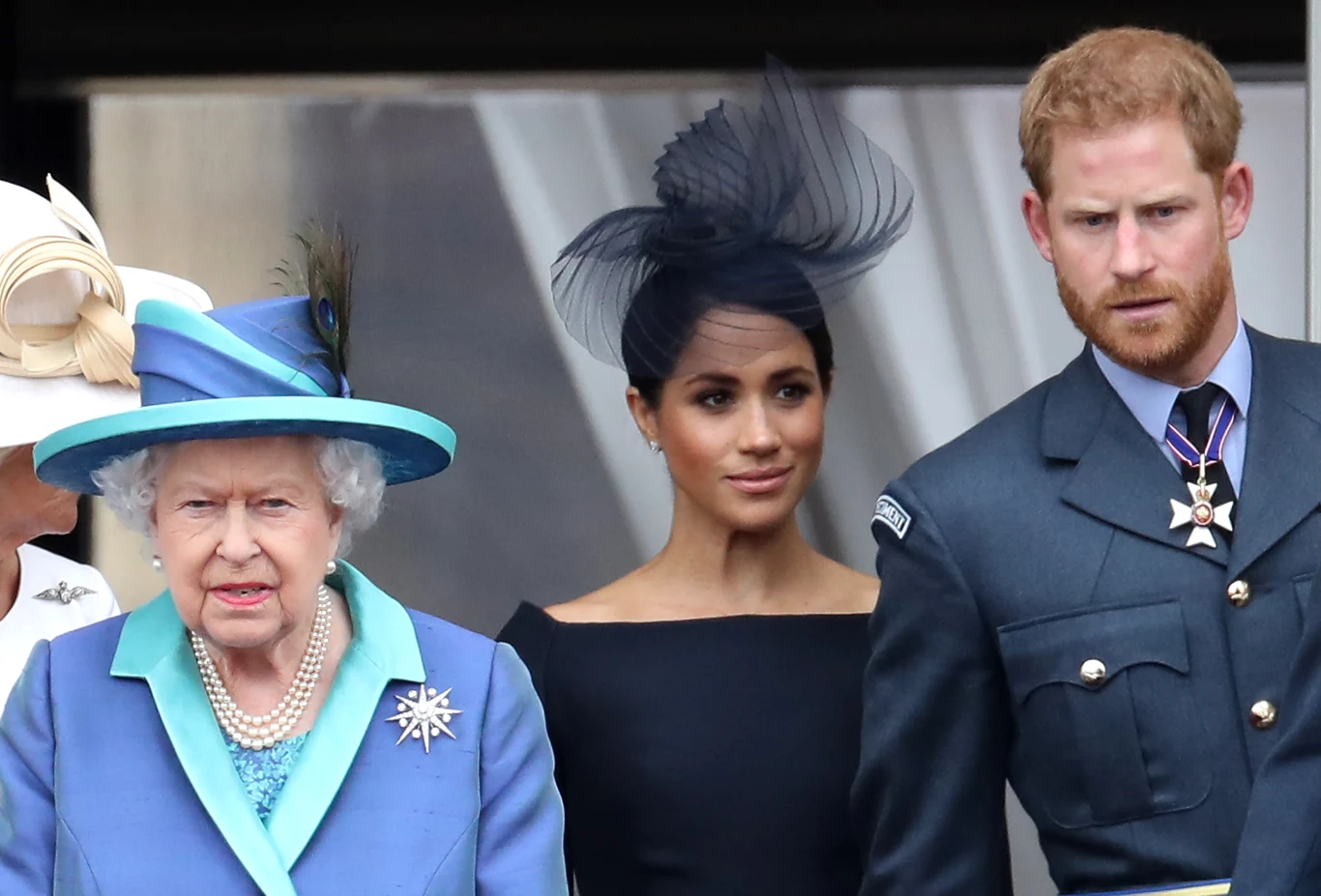 Czy Meghan i Harry chcieli się wyróżnić wybierając takie imię dla swojej córki? Trzy osoby w eleganckich, oficjalnych strojach, kobieta w niebieskim kapeluszu i płaszczu, druga kobieta w czarnej sukni z dekoracyjnym nakryciem głowy oraz mężczyzna w mundurze wojskowym z odznaczeniami.