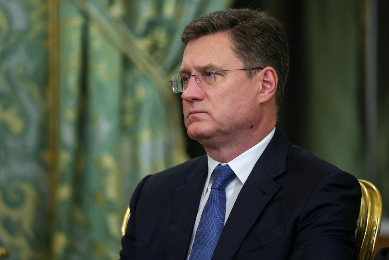Wicepremier Rosji Alekandr Nowak Wicepremier Rosji Aleksandr Nowak w garniturze i niebieskim krawacie siedzi na złotym krześle, w tle zielone zasłony.