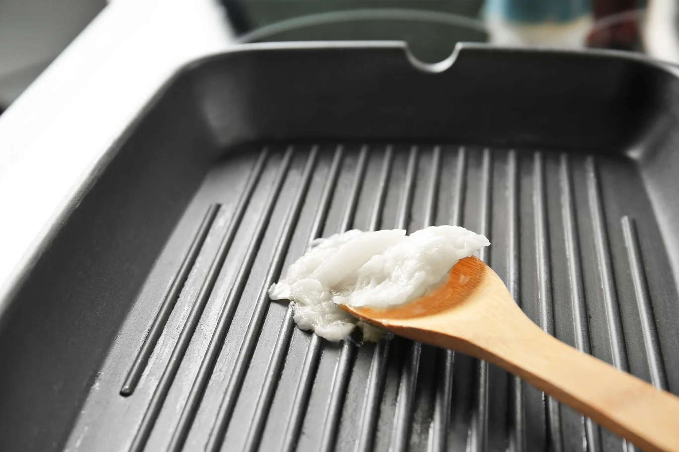 Porcja tłuszczu kokosowego nabierana drewnianą łyżką na żebrowaną, suchą patelnię grillową.