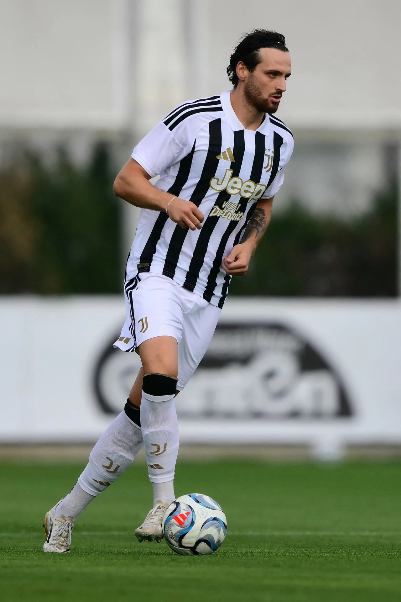 Federico Gatti Piłkarz w biało-czarnej koszulce Juventus Turyn prowadzi futbolówkę podczas meczu na zielonej murawie.