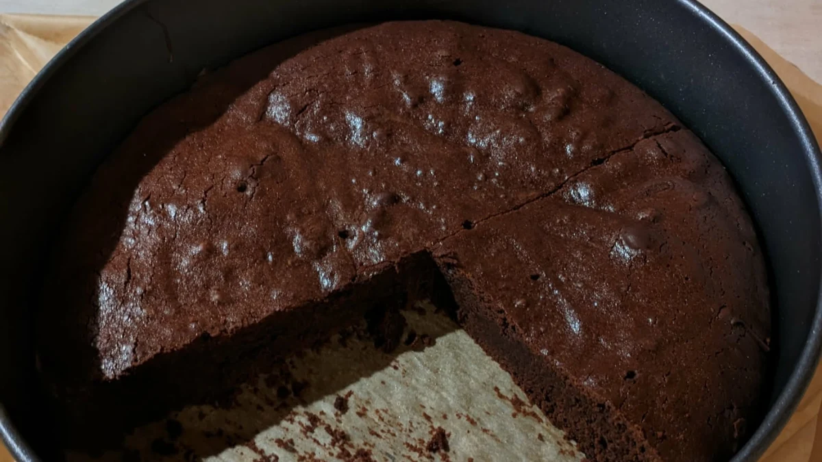 Proteinowe brownie wygląda i smakuje jak klasyczne ciasto Czekoladowe brownie proteinowe w okrągłej formie do pieczenia, z wyciętym jednym dużym kawałkiem.