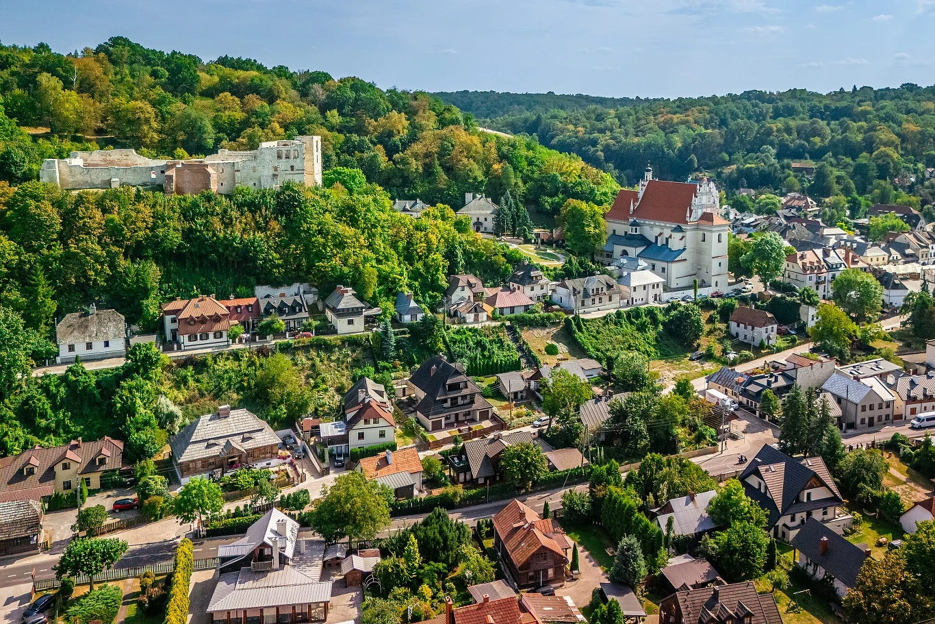 Lubelski Czek Turystyczny. Rusza rejestracja Panorama Lubelskiego z domami, zabytkowym kościołem o czerwonym dachu i ruinami zamku na wzgórzu. Dużo zieleni.