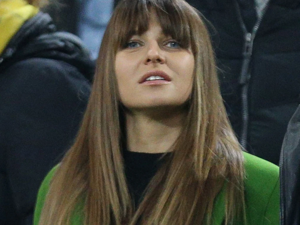 Anna Lewandowska Kobieta z długimi, prostymi włosami i grzywką, ubrana w zieloną marynarkę, patrzy w górę znajdując się wśród innych osób w tłumie.