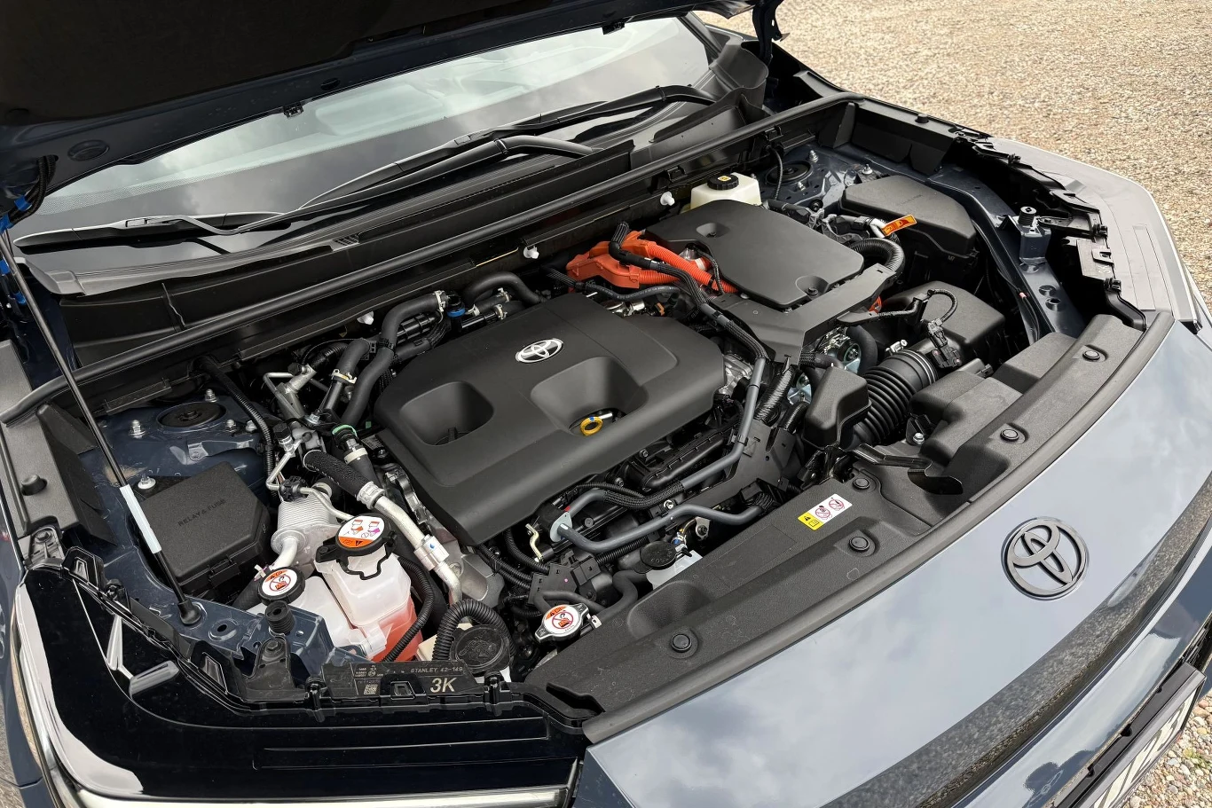 Komora silnika samochodu marki Toyota z wyeksponowanym silnikiem hybrydowym oraz widocznymi elementami elektrycznymi i osłoną silnika z logo producenta.