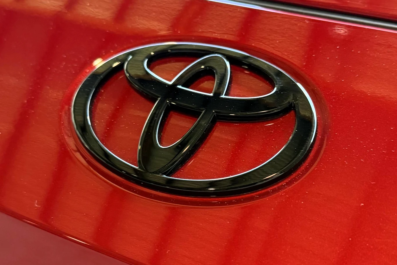 Czarny emblemat Toyoty umieszczony na błyszczącej, czerwonej powierzchni karoserii samochodu.