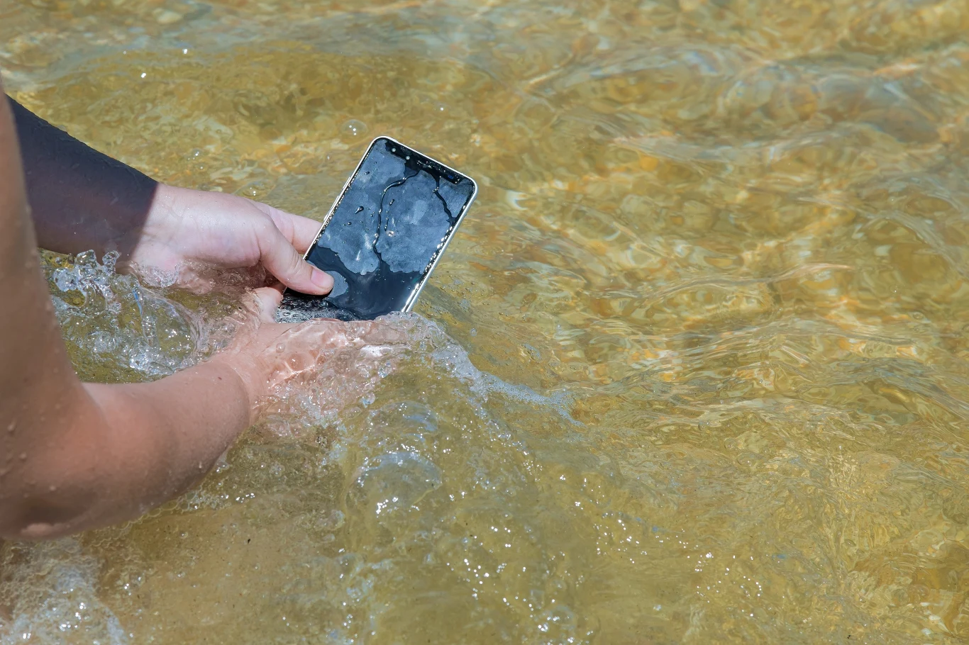 Zalany telefon? Możesz go jeszcze uratować, jeśli nie popełnisz tych kilku błędów Dwie dłonie trzymają smartfon częściowo zanurzony w przezroczystej wodzie.
