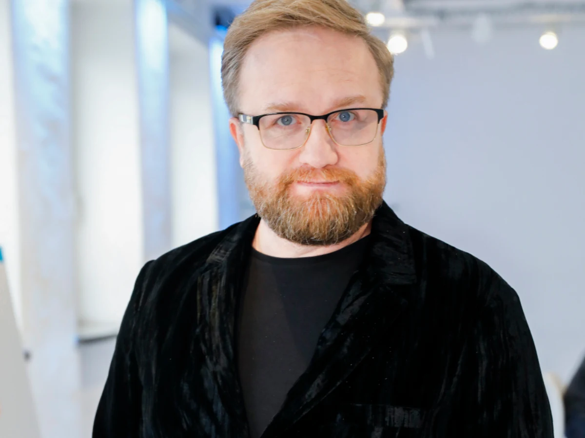 Bartłomiej Kasprzykowski Bartłomiej Kasprzykowski w czarnej marynarce i okularach pozuje w jasnym wnętrzu.