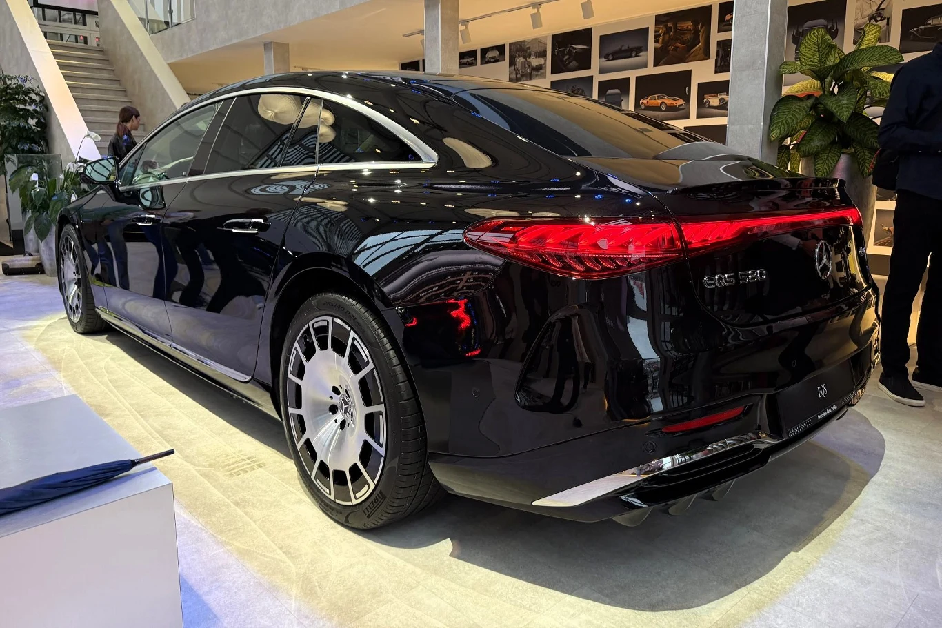 Mercedes EQS po liftingu mocno się zmienił - Niemcy deklarują, że wymienili lub zmodernizowali ponad jedną czwartą podzespołów. Mercedes-Maybach EQS 580 po liftingu, czarny, z czerwonym pasem tylnych świateł, w salonie motoryzacyjnym