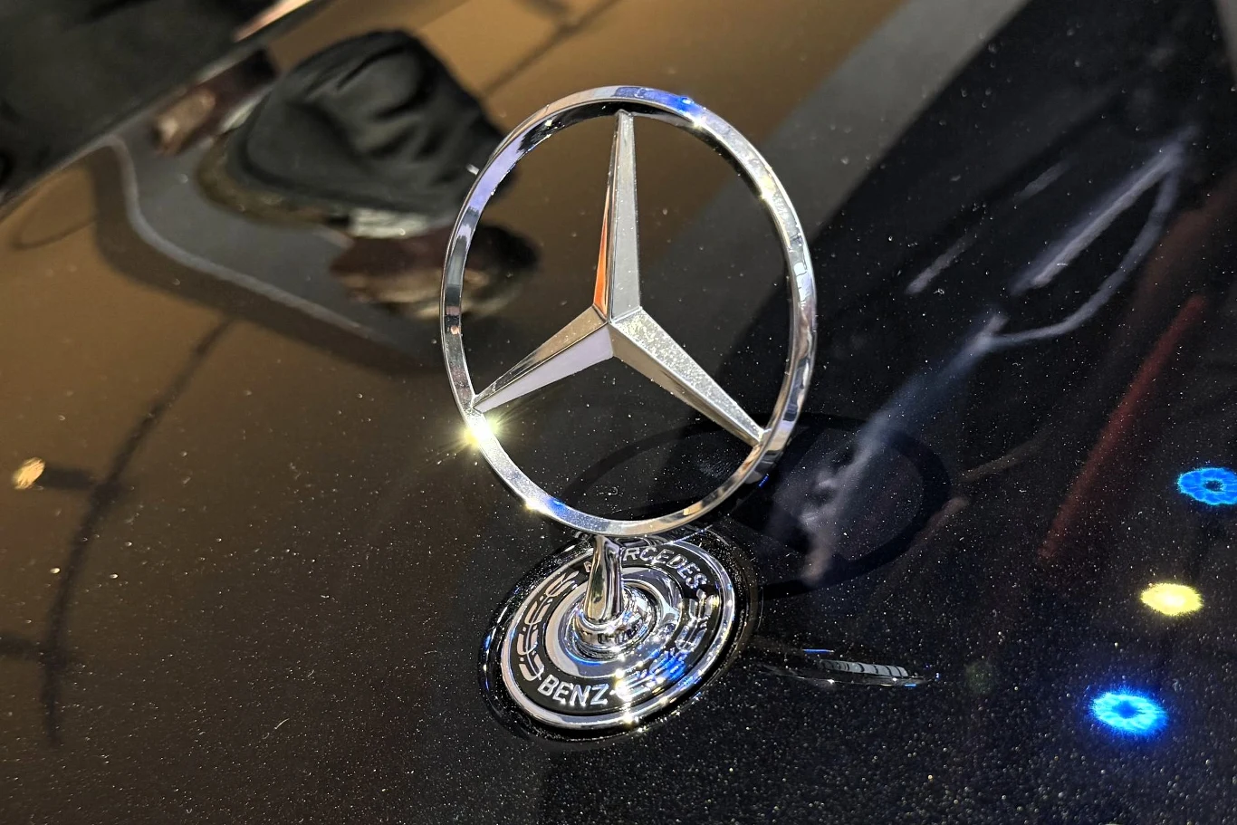 Ceny Mercedesa EQS po liftingu zaczynają się od 499 900 zł. Chromowany emblemat Mercedes-Benz umieszczony na błyszczącej masce samochodu, otoczony refleksami świetlnymi.