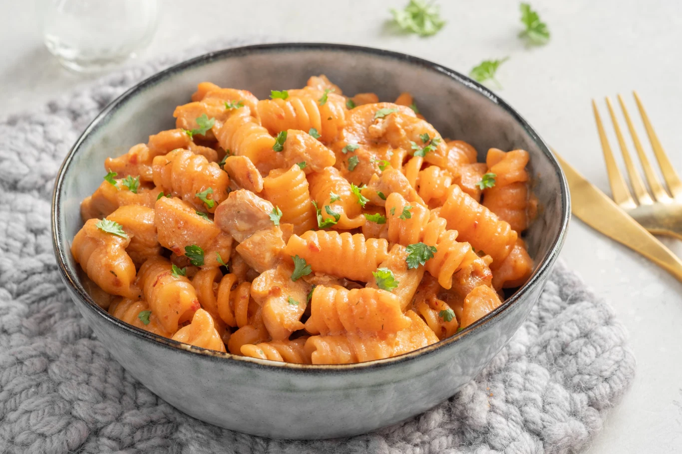 Miska makaronu fusilli w kremowym sosie pomidorowym z kawałkami kurczaka i posypką z natki pietruszki.