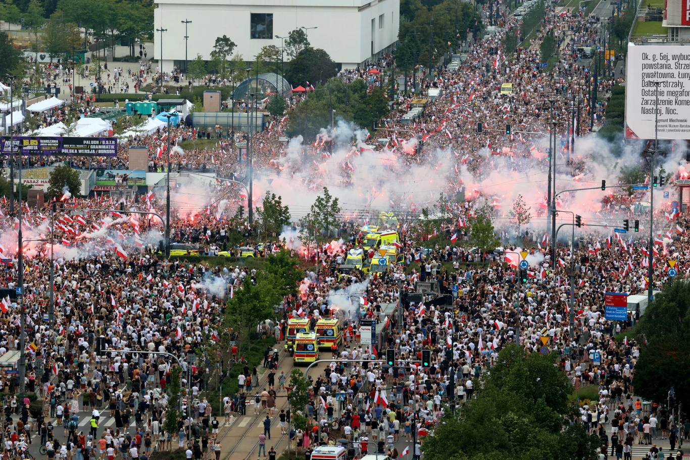 Obchody 82. rocznicy wybuchu Powstania Warszawskiego Tłum z biało-czerwonymi flagami i racami na ulicy, obok karetek pogotowia i radiowozów.