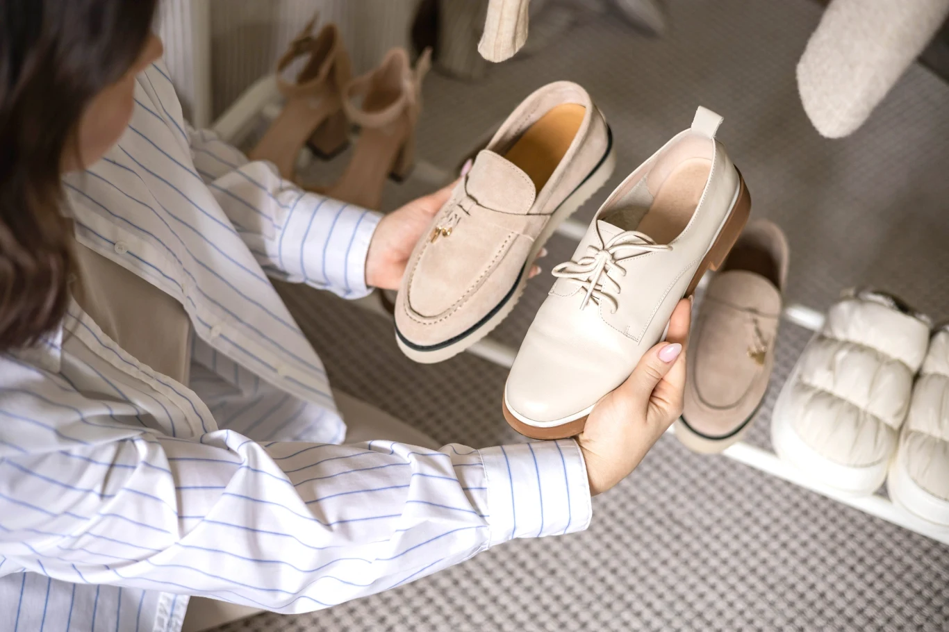 Moda 2026 wraca do lat retro Osoba w jasnej koszuli trzyma w rękach dwa jasne buty, porównując ich wygląd i styl, na półce widoczne są inne pary eleganckich butów w stonowanej kolorystyce.