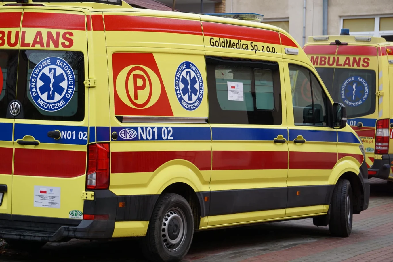 40-latka zginęła pod kołami auta w Lipowej (zdjęcie ilustracyjne) Dwa żółto-czerwone ambulanse przy budynku, stojące obok siebie na parkingu, zdjęcie ilustracyjne