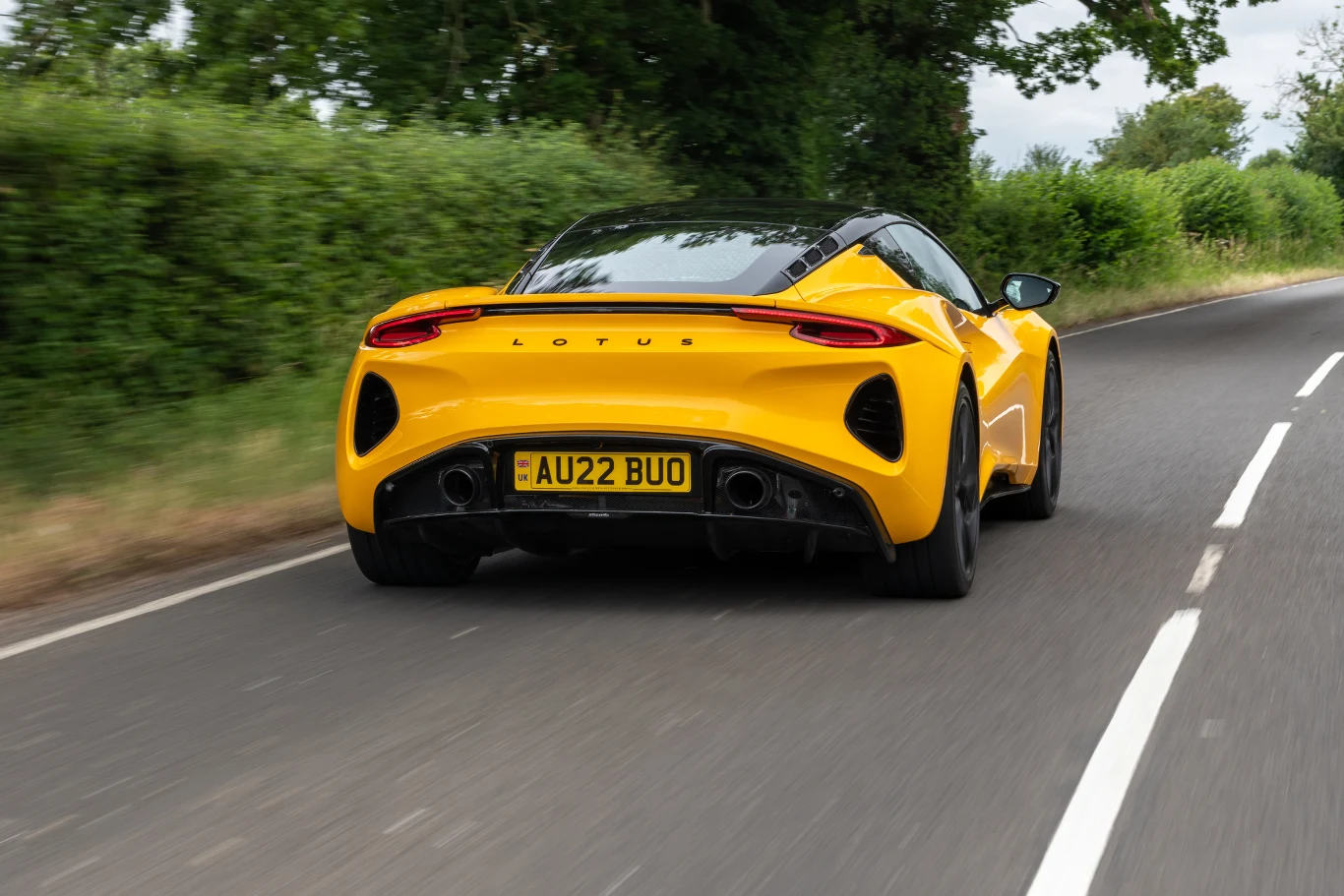 Lotus Emira dostępny jest wyłącznie z silnikiem spalinowym. Żółty sportowy samochód Lotus porusza się asfaltową, krętą drogą otoczoną zielonymi krzewami.
