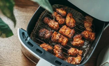 Kawałki kurczaka pieczone w koszu air fryera na drewnianym blacie 