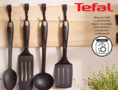 Kuchenne przybory Tefal od 39,99 zł Cztery czarne przybory kuchenne marki Tefal, w tym chochla, dwie łopatki i łyżka, zawieszone na drewnianym uchwycie na ścianie.
