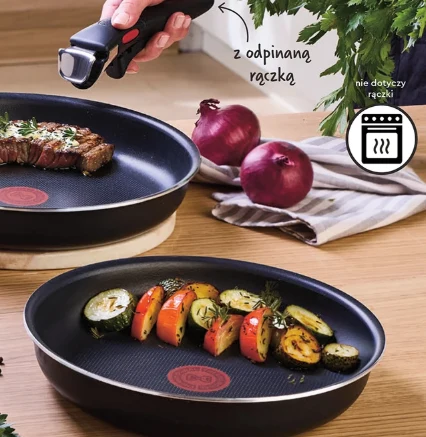 Zestaw patelni Tefal za 169 zł Dwie czarne patelnie z systemem odpinanej rączki, jedna z grillowanym stekiem z ziołami, druga z pieczonymi warzywami; w tle czerwone cebule i natka pietruszki.