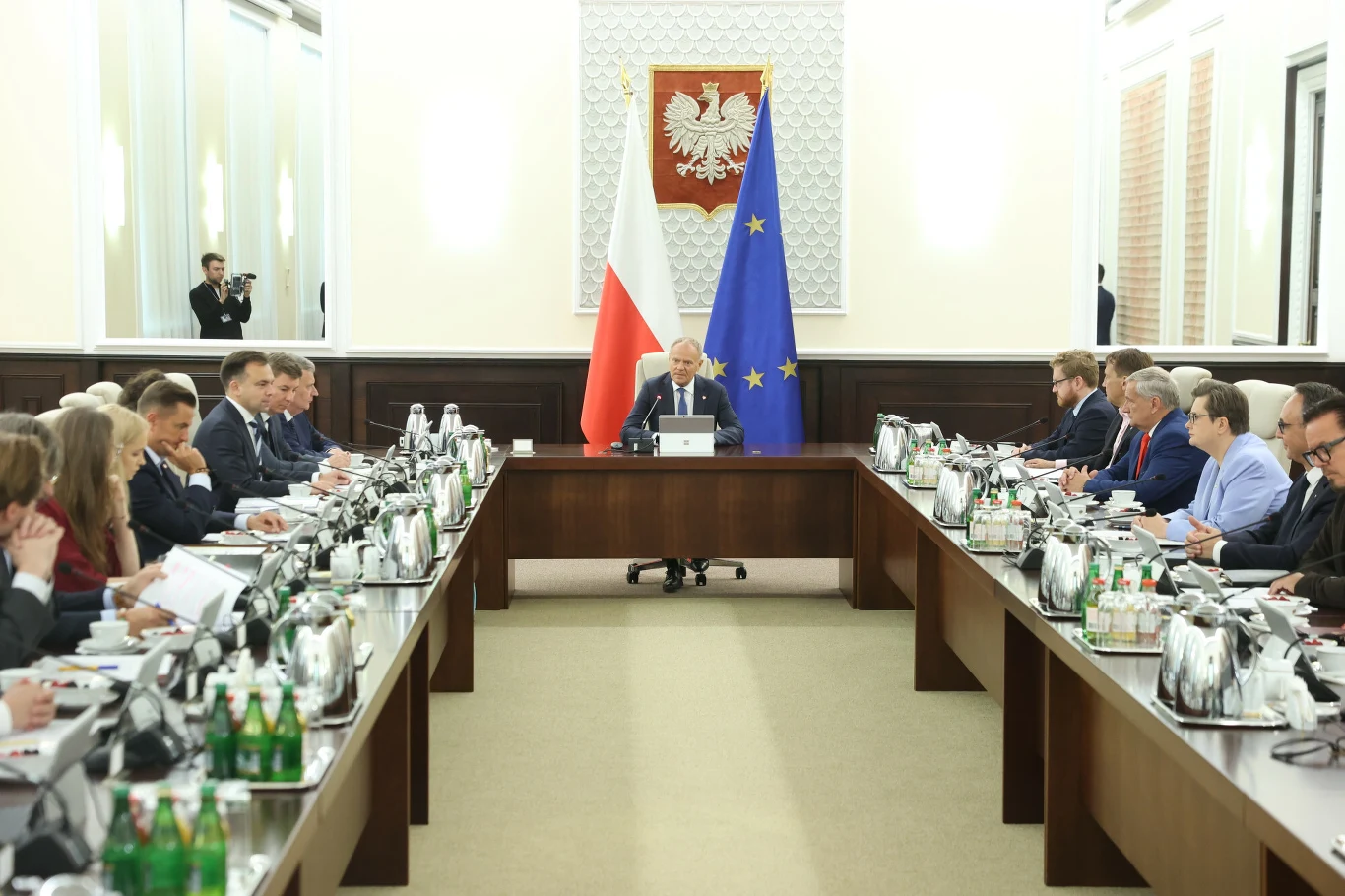 Jest decyzja rządu ws. zmian w podatkach Posiedzenie rządu przy długim stole, flagi Polski i UE, godło państwowe na ścianie.