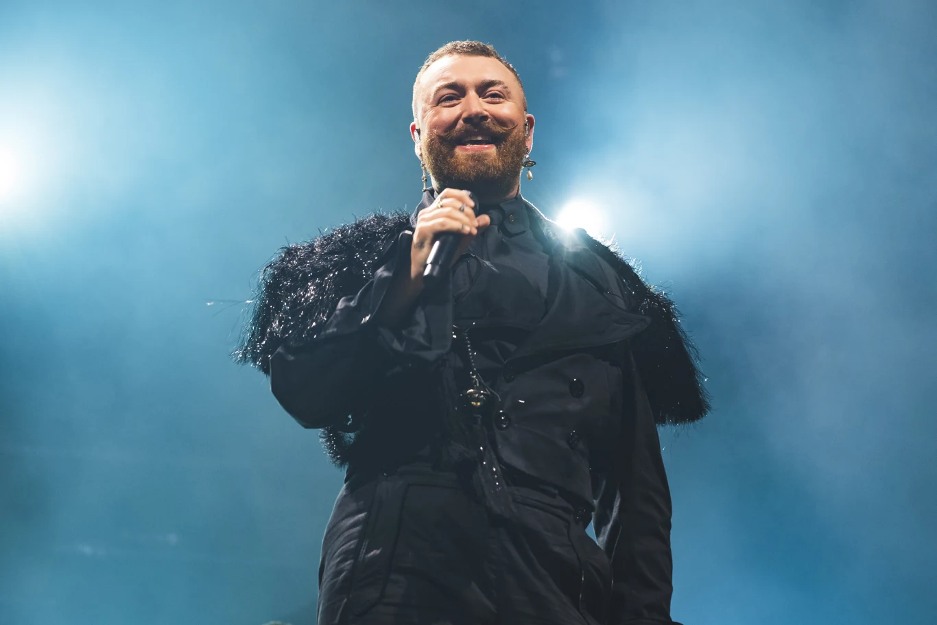 Sam Smith w 2022 r. wypuścił hit "Unholy" Sam Smith w czarnym, stylizowanym stroju z mikrofonem na oświetlonej scenie podczas występu.