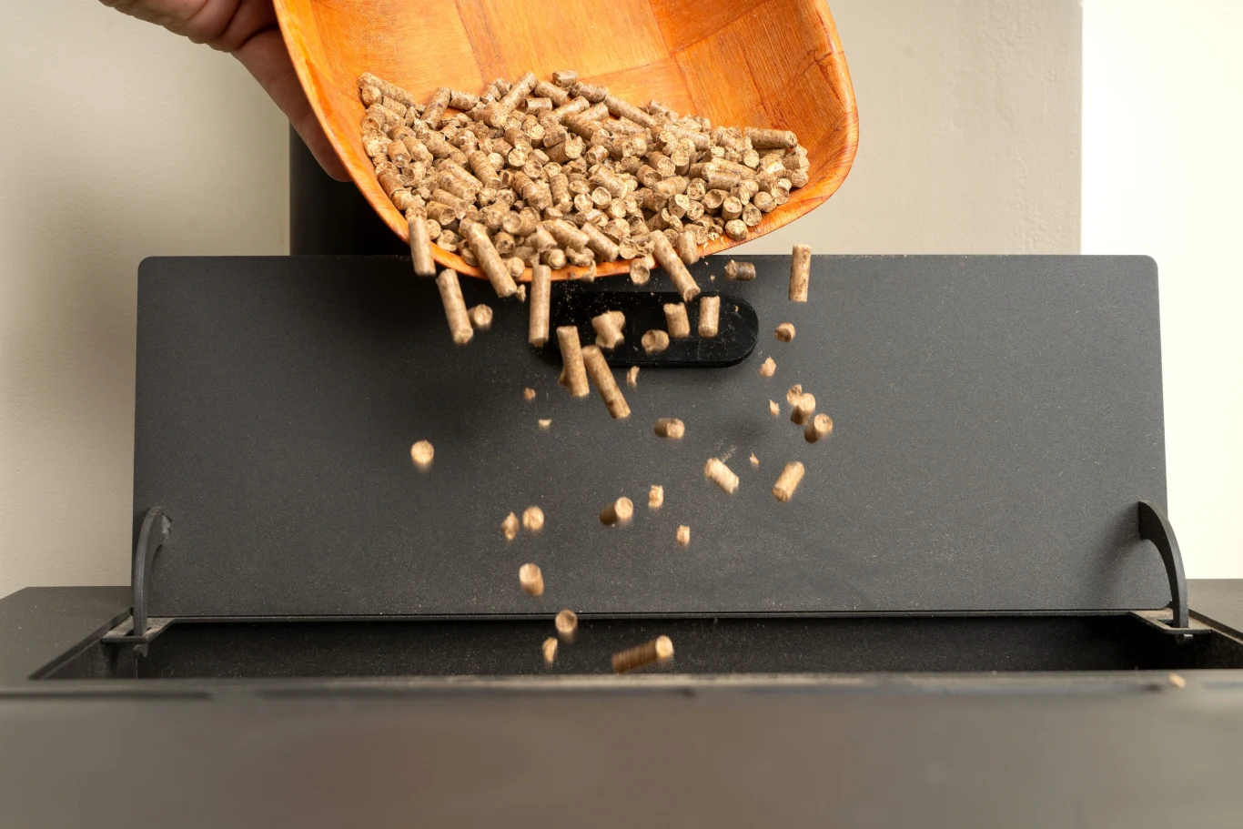 Czy opłaca się latem kupić pellet na zapas? Ręka wsypująca drewniane pellet do otwartego zasobnika pieca lub kotła na pellet.
