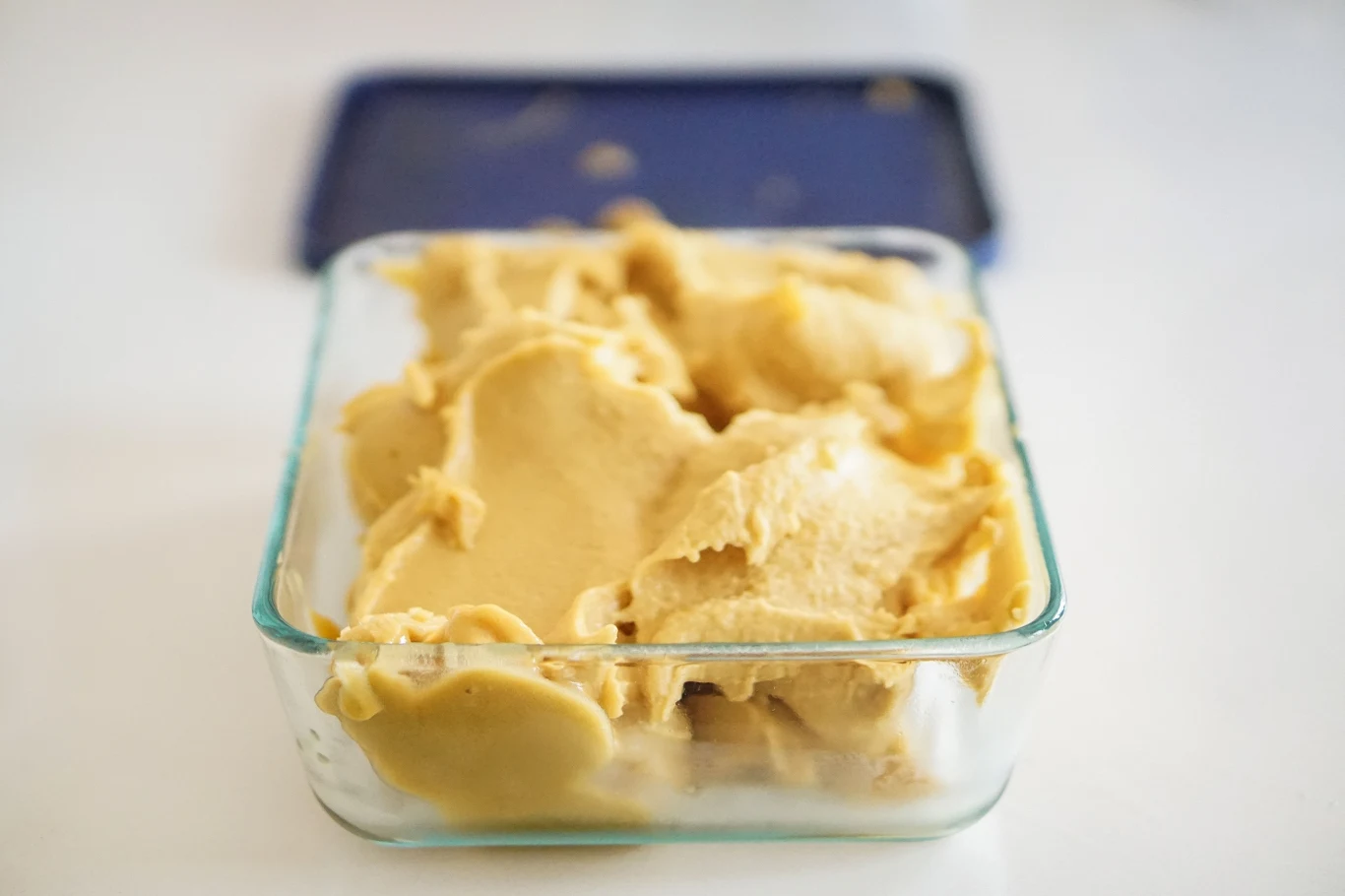 Pasta miso jest dostępna w większych marketach i specjalistycznych sklepach azjatyckich Porcja jasnej pasty miso w przezroczystym pojemniku z niebieską pokrywką na tle sklepowym.