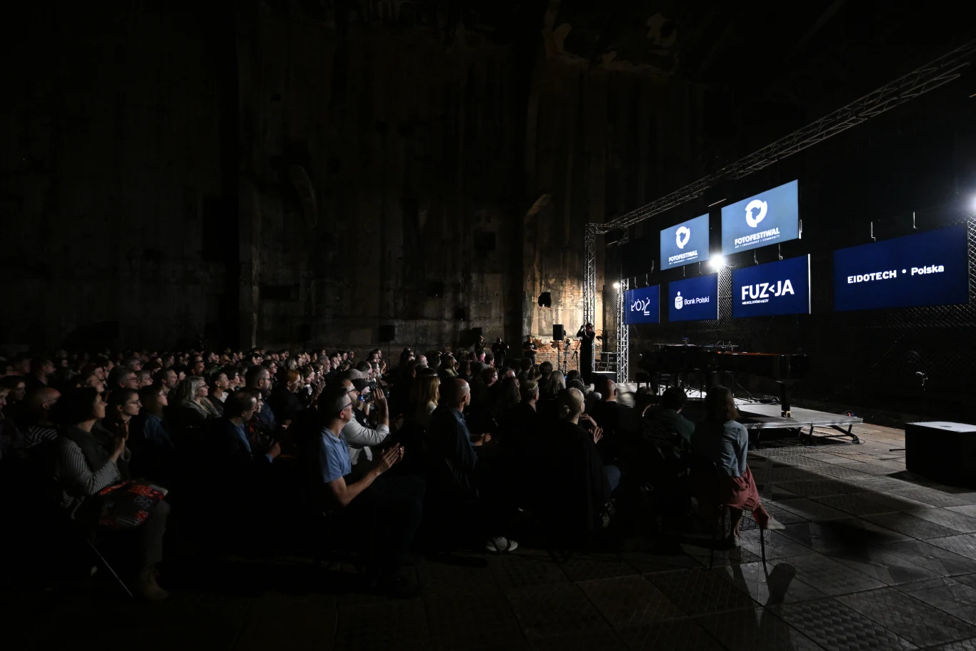 Koncert Hani Rani Sala wypełniona publicznością skupioną na dużych ekranach na scenie, na których wyświetlane są prezentacje dotyczące wydarzenia Fuzja oraz Edutech Polska.