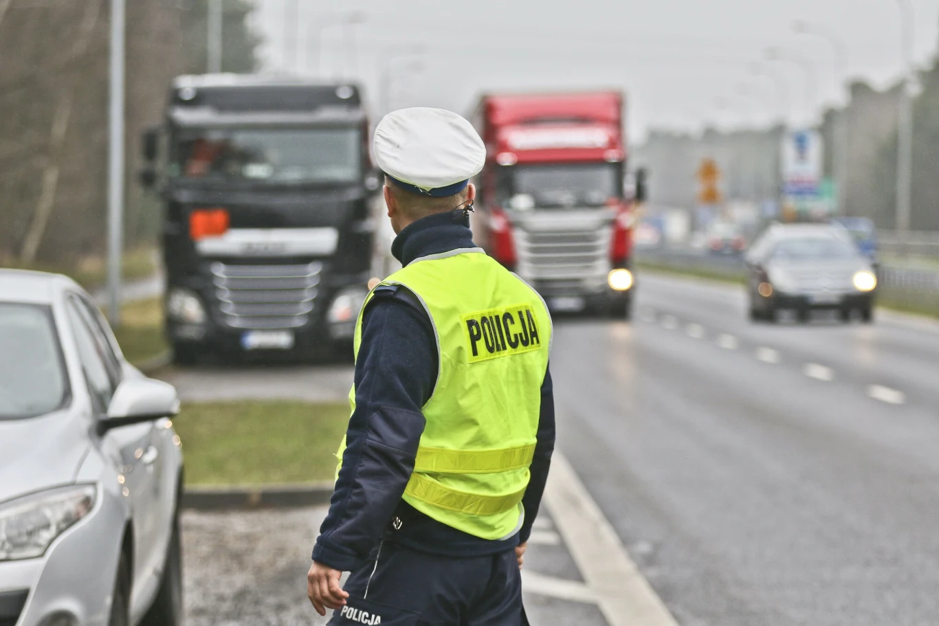 Zakaz jazdy dla ciężarówek. Zostały tylko dwa weekendy. Policjant w odblaskowej kamizelce obserwuje jadące ciężarówki na ruchliwej drodze podczas wakacyjnych ograniczeń.