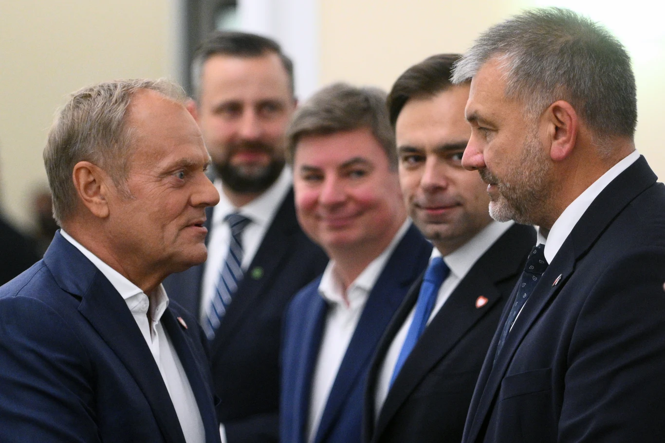 Premier Donald Tusk i minister sprawiedliwości Waldemar Żurek odegrają kluczowe role w bitwie o Trybunał Konstytucyjny Grupa elegancko ubranych mężczyzn w garniturach prowadzi rozmowę twarzą w twarz, skupiając uwagę na najstarszym z nich o blond włosach po lewej stronie obrazu.