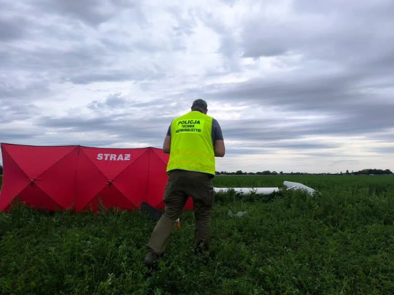 Katastrofa szybowca w Lesznie, zginął pilot Policjant w żółtej kamizelce idzie przez pole w stronę namiotu i fragmentów białego szybowca w Lesznie