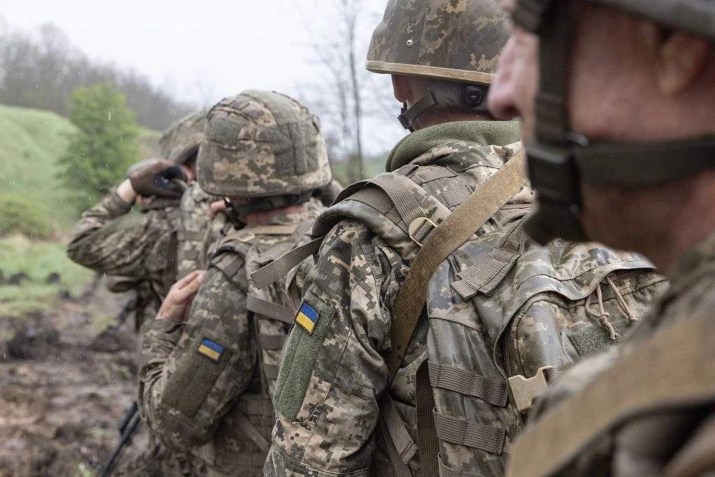 Ukraina. Atak na żołnierza we Lwowie. Mężczyzna nie przeżył Ukraińscy żołnierze w umundurowaniu i hełmach stoją w szeregu na wilgotnym polu, widoczne flagi Ukrainy.