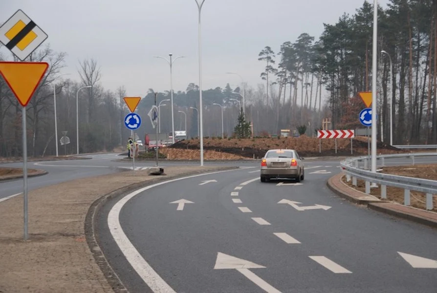 Dla części kierowców pokonanie ronda jest problemem Samochód zbliżający się do ronda z barierami ochronnymi, znaki pierwszeństwa i ruch okrężny, w tle drzewa