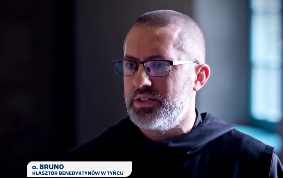 O. Bruno Mężczyzna w okularach i habicie benedyktyńskim, z widocznym krótkim zarostem, przemawia w jasnym pomieszczeniu.