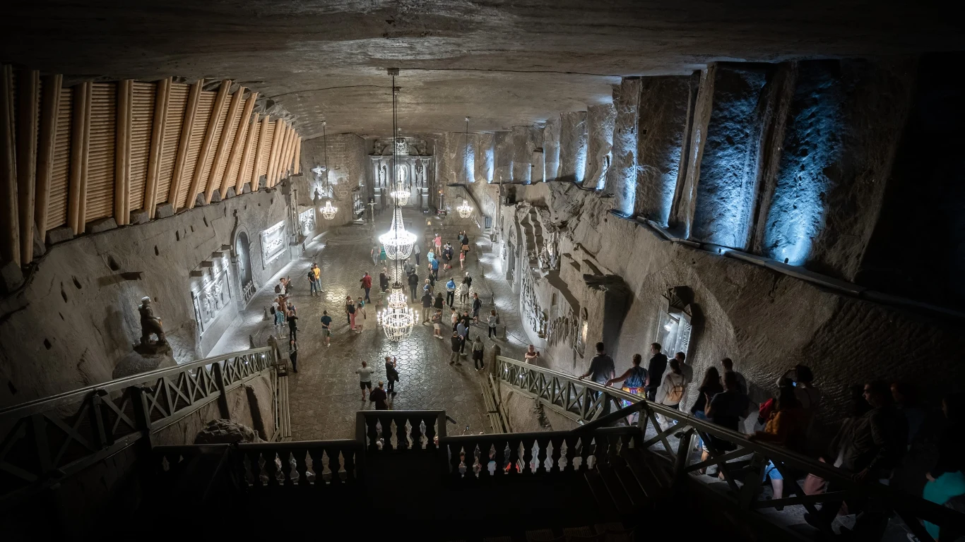 Komnata wykuta w skale z żyrandolami, rzeźbami i licznymi detalami architektonicznymi podświetlonymi światłem, w której przechadzają się grupy ludzi.