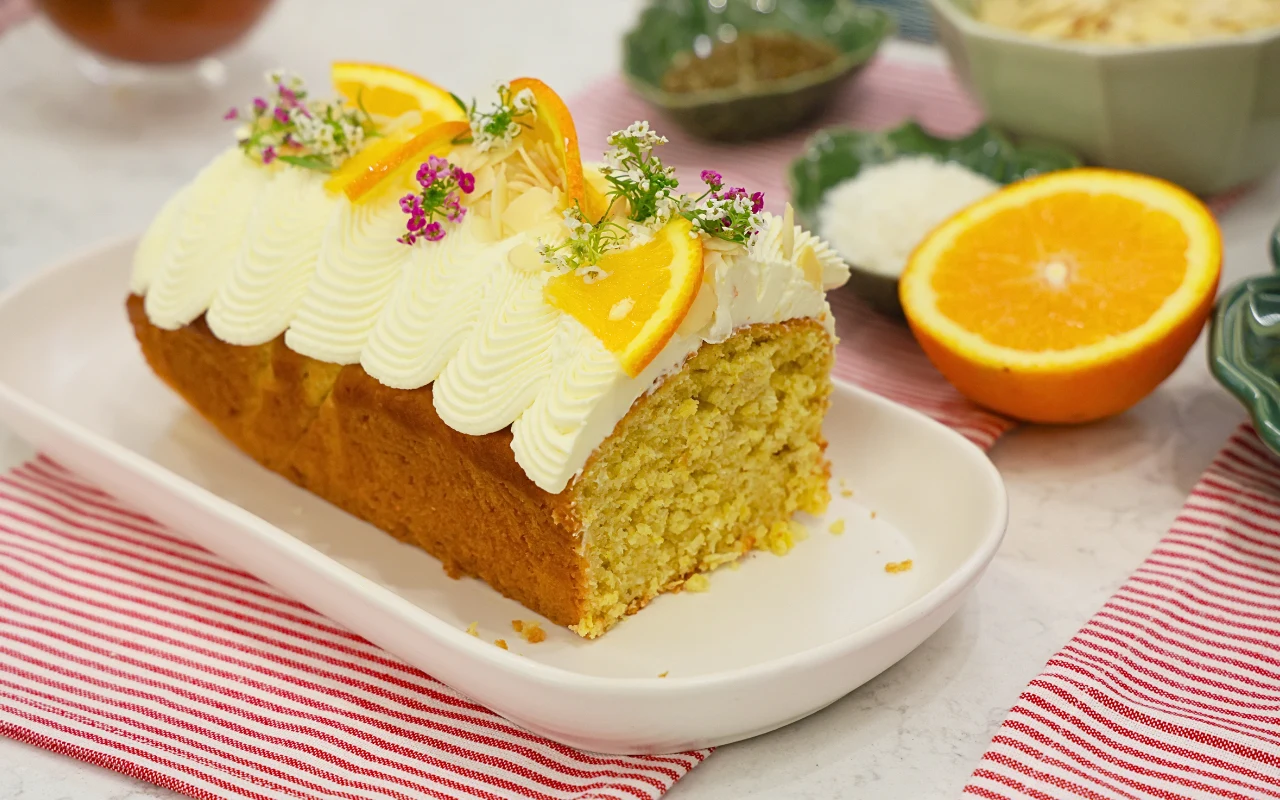 Ciasto kukurydziane z pomarańczowym kremem na bazie mascarpone i białej czekolady Kukurydziane ciasto z kremem mascarpone i białą czekoladą, ozdobione pomarańczą i kwiatami na białej tacy