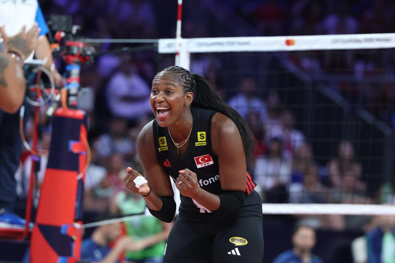 Sinead Jack-Kisal, środkowa reprezentacji Turcji Zawodniczka siatkarskiej reprezentacji Turcji w czarnej koszulce energicznie celebruje punkt podczas meczu, stojąc blisko siatki na hali sportowej.
