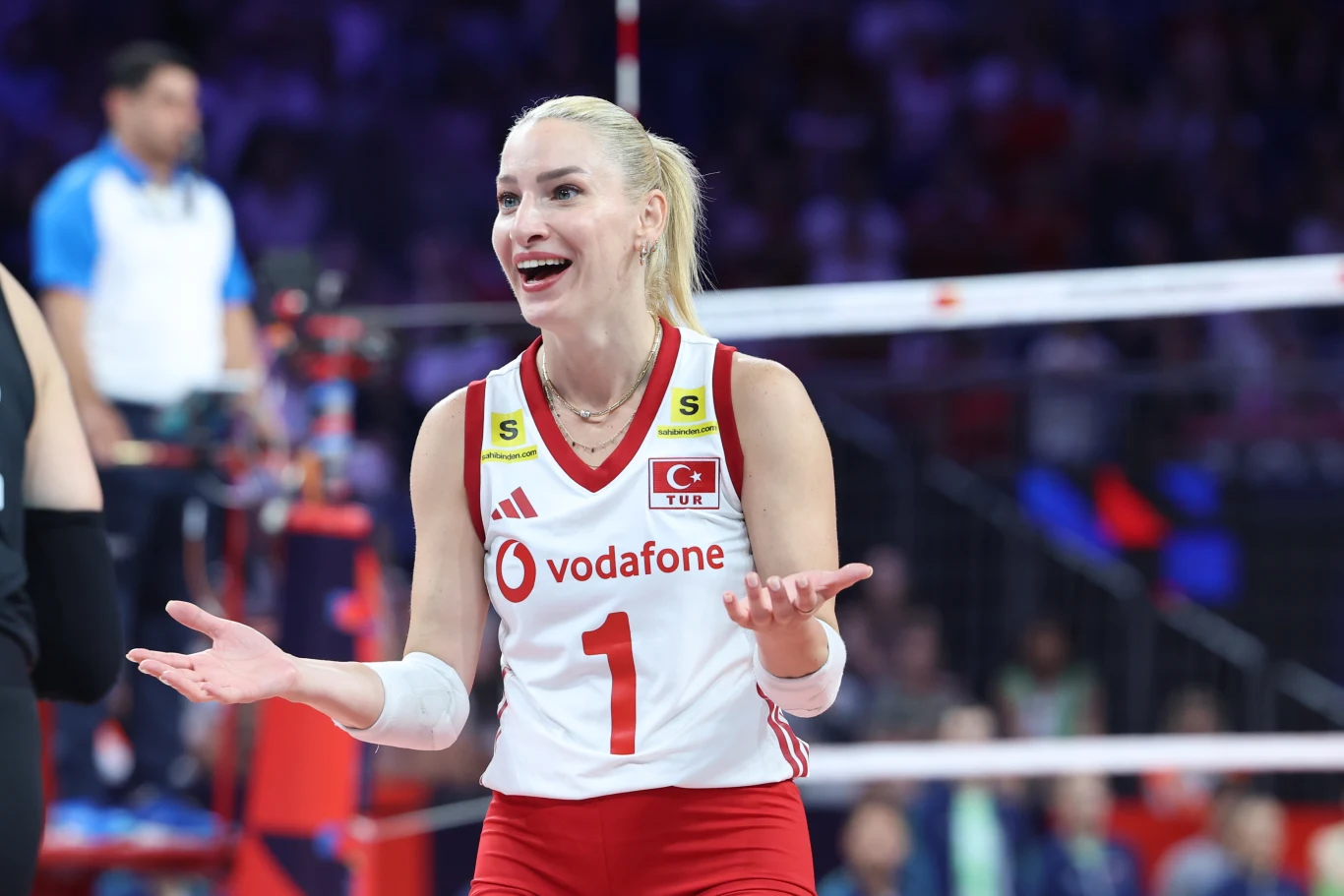 Gizem Orge, libero reprezentacji Turcji Gizem Orge, libero Turcji, w biało-czerwonym stroju z numerem 1 i turecką flagą, gestykuluje na boisku siatkarskim.