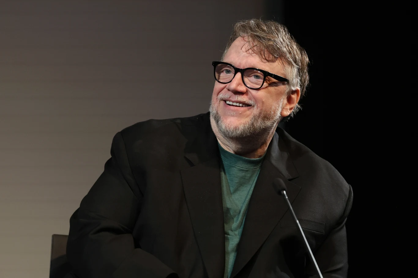 Guillermo del Toro w 2026 roku Uśmiechnięty mężczyzna w okularach i czarnej marynarce siedzi przy mikrofonie na jasnym tle.